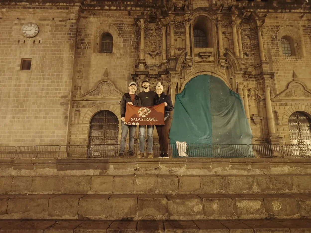 Salas Travel travelers holding the company banner in front of Cusco Cathedral at night