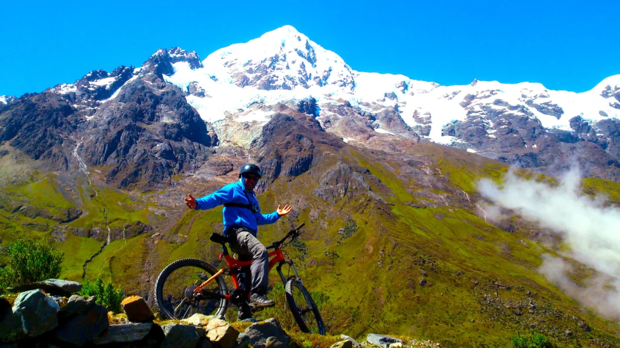 Cyclist celebrating below a snow-capped mountain on the Inca Jungle bike descent