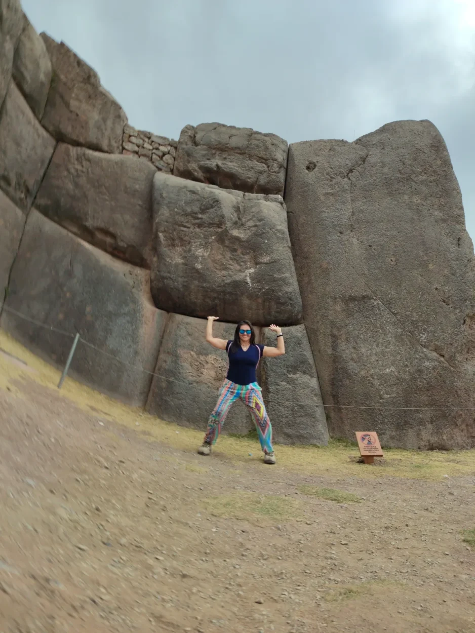 Traveler posing under a giant stone at Sacsayhuamán